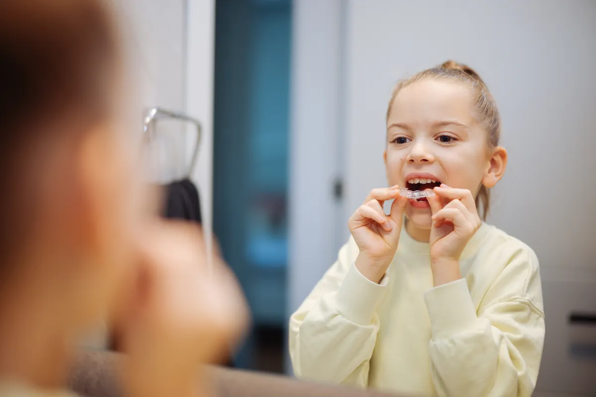 Young girl placing a clear aligner into her mouth in front of a mirror