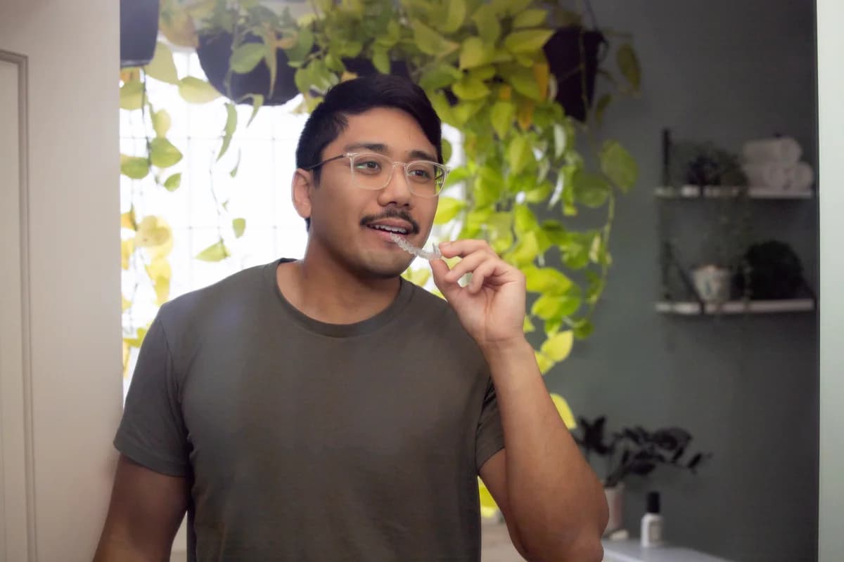 Person holding a clear aligner next to fixed braces for comparison