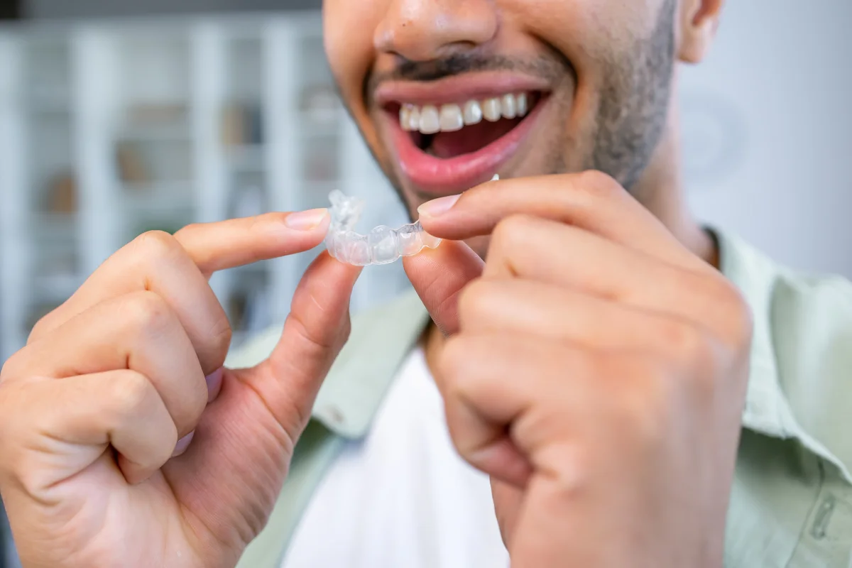 Person holding a clear removable retainer after finishing orthodontic treatment